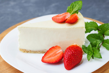 Classic cheesecake New York sliced Piece of cheesecake with fresh strawberries and mint on a white plate on a classic blue background. Close up. Selective focus. Copy space