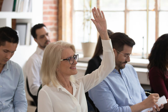 Middle Aged Woman Raising Hand To Ask Question At Seminar