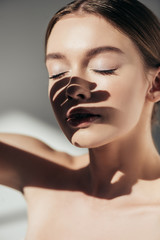 portrait of nude girl with closed eyes and shadows on face on grey