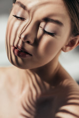 Naklejka premium portrait of naked girl with closed eyes and shadows on face on grey