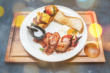 Breakfast Bacon Ham Egg Honey bread, strawberry with syrup and dried chili Served in a white plate, placed on a wooden tray on a black marble table. Image contain grain or noise and soft focus bokeh.