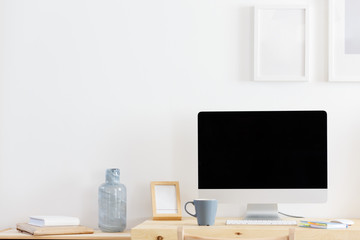 Cozy empty workplace at home or in the office is a desk and a computer with a large empty black screen standing next to the mug. Remote and freelance work concept. Advertising space