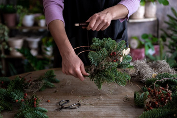 Fototapeta premium Woman making Christmas wreath of spruce, step by step. Concept of florist's work before the Christmas holidays..