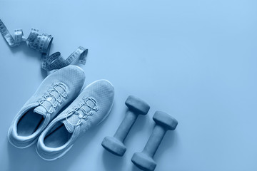 Sport and fitness equipment, dumbbells, fitness shoes, measuring tape on blue. Top view, space for...