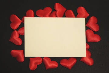 Valentine's Day card mockup surrounded by small fabric hearts. Flat lay photo on black background, with text space.