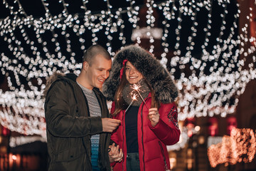 Obraz premium Young man and his girlfriend are having fun with sparklers , at night