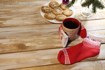 Warm hug of christmas sock with hot coffee with wooden background, fir tree branch and new year cookies