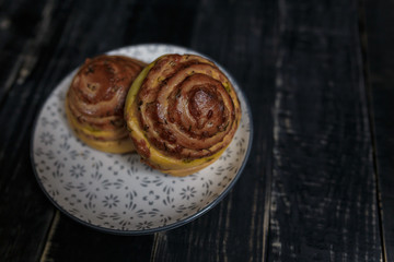 Fototapeta premium Two cheese and dill bread buns on plate standing on black wooden background. Tasty unhealthy food. Diet, nutrition, eating habits concept. Place for text. 