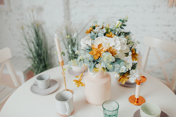 White dining room interior design. White round table with flowers, candles and cups.