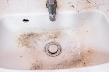 Very dirty hands wash basin including metal drain and water tap.