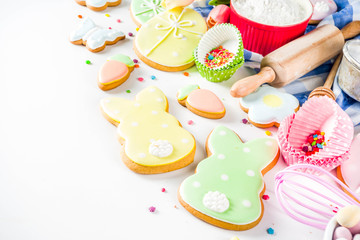 Sweet Easter baking cooking background with traditional Easter bunny and egg cookies, sugar sprinkles, ingredients, utensils. White table background copy space layout