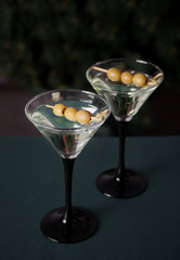 Two glasses of martini with olives on the dark background.