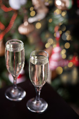 Two glasses of champagne nearby Christmas tree with bokeh