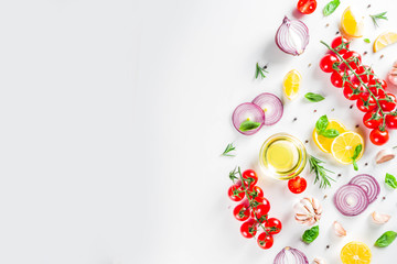 Cooking background with spices, vegetables and herbs fresh basil, rosemary, tomato, garlic, onions, lemon on a white kitchen table. Layout top view copy space. Healthy ingredients for cooking