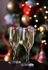 Two glasses of champagne nearby Christmas tree with bokeh