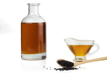 Black cumin seeds on a wooden spoon and black seed oil in a glass bottle and gravy boat. Isolated on white background.