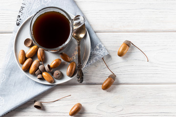 Hot coffee made from acorns in a glass with a napkin is a tonic drink with a coffee flavor, rich color and pleasant aroma. On a white wooden background