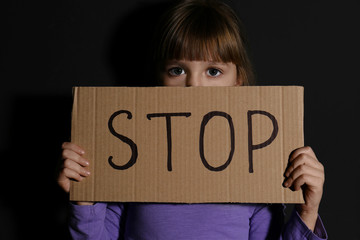 Abused little girl with sign STOP near black wall. Domestic violence concept