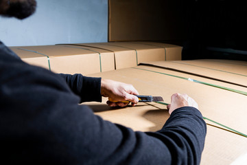 Man using an utility knife to open a cardboard box. Opening packages in a warehouse. Unboxing.