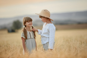 Naklejka na ściany i meble A boy in a straw hat and a girl with two pigtails stand knee deep in a field of wheat.