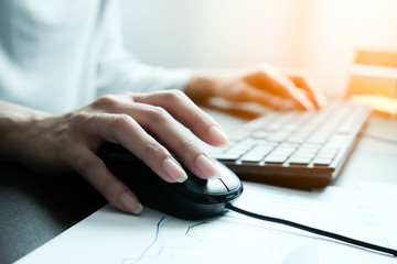 Asian woman's hand beauty, long nails, pressing on mouse and typing the text on a black computer keyboard. On the table have graph of reports, Maybe analyse data for preparing for a marketing meeting