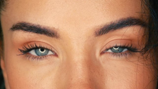Beautiful eyes of young curly brunette woman with professional ring light looks straight into the frame. Cute girl with blue eyes close-up circular light