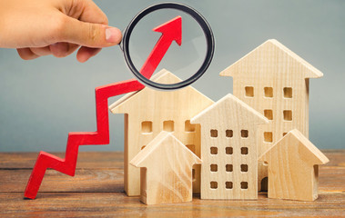 Miniature wooden houses and red arrow up. The concept of increasing the cost of housing. High...