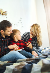 Christmas family in Christmas Santa hats. Dad, mom and son spending time together, eating marshmallow in the bed at home. Young family celebrating Christmas and New Year, having fun, happy time