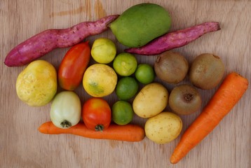 Vegetables, fruits and starches on wooden background. Potatoes, kiwi fruit, carrots, mango, tomatoes, limes and passion fruit. Healthy food concept.