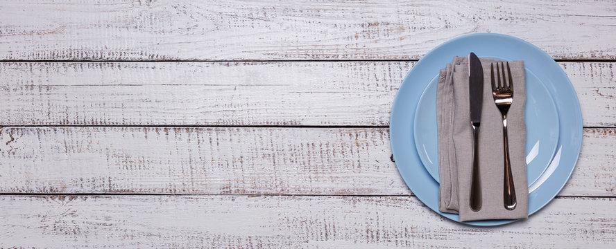 Blue plates, napkin and cutlery on an old white wooden background.