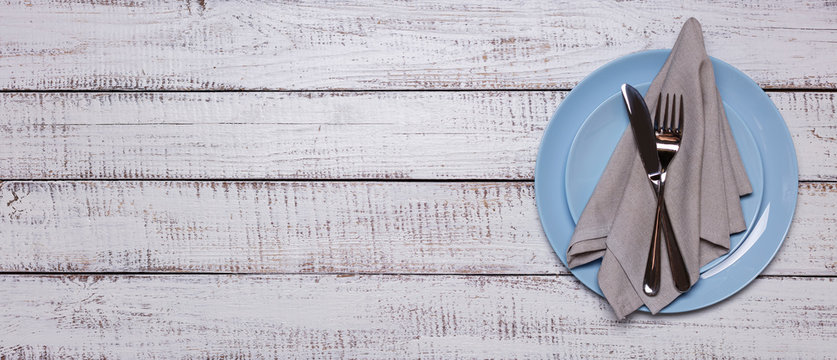 Blue plates, napkin and cutlery on an old white wooden background.