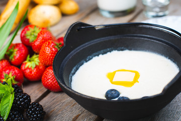 Traditional breakfast milk porridge with butter and berries on a wooden table.