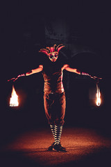 Man in red jester costume with holding double fire chains making some action moment, standing in the dark - obrazy, fototapety, plakaty