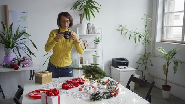 Female photographer arranging objects on table in studio and photographing Christmas flatlay with professional camera