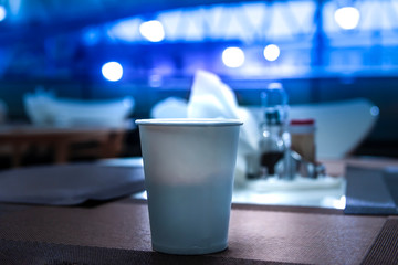 White glass of paper for coffee or tea, standing on the table against the background of blue lights. Light of the year concept. Space for text.