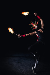 Man in red jester costume with double fire torch performing some action moment stand with one leg...