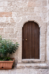 Fototapeta na wymiar Arched entrance to the building. Stone portal, closed wooden door, porch and plants. Monopoli, Italy.