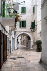 Fototapeta na wymiar Narrow deserted street, stone walls and arches. Windows, doors, balcony. Monopoli, Italy.