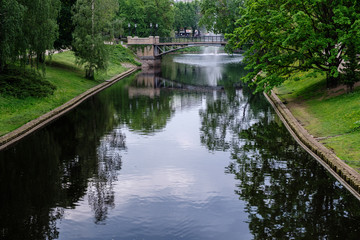 City canal, bridge and fountain, reflections in the water. Trees on the banks. Spring, Riga, Latvia.