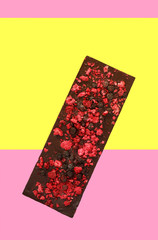 Chocolate with dried red berries on pink yellow background