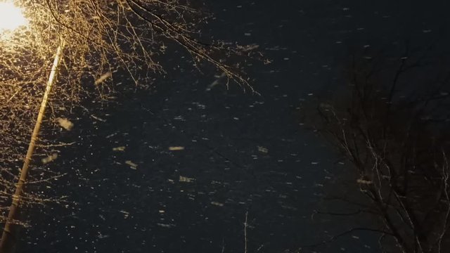 Snowfall against the background of the night sky and a yellow lantern