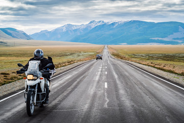 A motorcyclist with his hand raised in greeting, riding along the Chuysky highway at dawn, landscape with a highway. Russia, mountain Altai