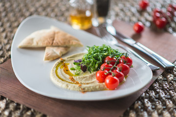 Traditional appetizer hummus with bread cakes, pita, on a plate with vegetables and sauce.