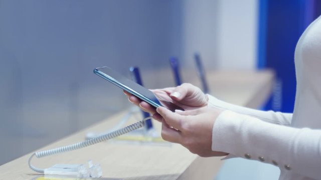 Woman chooses a smartphone in an electronics store, close-up. She takes smart phone from counter and trying using it.