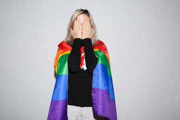 Young lesbian woman with rainbow flag hiding her face. Alone and sad girl.