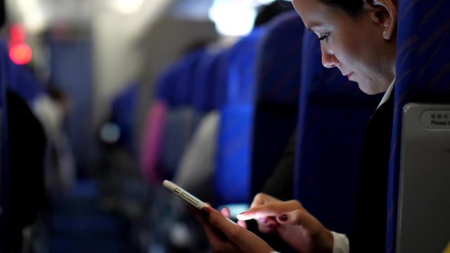 Woman texting smartphone during flight, type answer using instant messenger application. Blurred aisle of economy class cabin. Short international flight at East Asia
