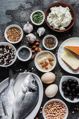 Source of calcium in products - fish, sesame, cheese, cottage cheese, poppy seeds, olives, flax seeds, eggs, legumes, almonds, garlic on a dark background, top view