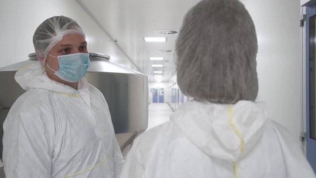 Man and woman employees talking while standing in pharmaceutical company during working day. Two people discussing work, having break time in interior with industrial equipment. Professional staff is