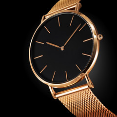 Close up of an expensive wristwatch made of gold metal and isolated on a black background