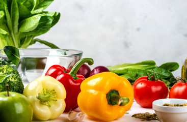 Multi-colored peppers and various vegetables and spices on the table. Ingredients for cook salad on a light background with place for text. Healthy diet vegan food concept.
